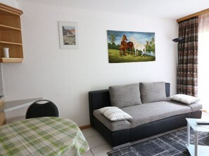 A living room with a sofa, a table with a checkered tablecloth, a painting of horses, and a window with curtains. - Adlerhorst Leukerbad # 2-bed apartment, Dusche, WC by Interhome (Leukerbad)