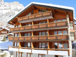 A multi-story wooden building with balconies, set against a snowy mountain backdrop. - Adlerhorst Leukerbad # 2-bed apartment, Dusche, WC by Interhome (Leukerbad)