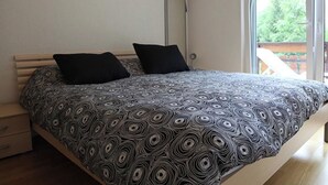 A bedroom with a bed, two pillows, a floor lamp, and a view through a large window. - Edelweiss D 02 # 4-bed apartment, Dusche, WC 4-Bettwohnung, Dusche, WC by Interhome (Leukerbad)
