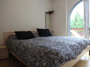 Ein Schlafzimmer mit einem Bett, zwei Kissen, einer Stehlampe und Blick durch ein großes Fenster.