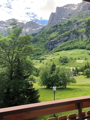 Eine gebirgige Landschaft mit einem Wasserfall, üppiger Vegetation und einer Holzterrasse.