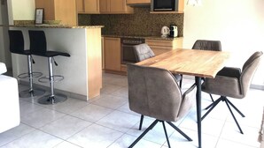 A compact kitchen with a dining area, featuring a wooden table, grey chairs, a built-in oven, and a microwave. - Edelweiss D 02 # 4-bed apartment, Dusche, WC 4-Bettwohnung, Dusche, WC by Interhome (Leukerbad)