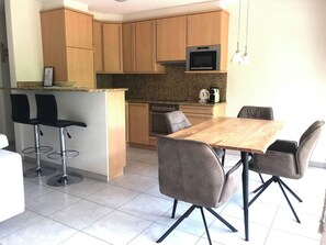 Eine kompakte Küche mit Essbereich, ausgestattet mit einem Holztisch, grauen Stühlen, einem eingebauten Backofen und einer Mikrowelle.