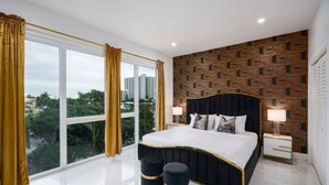 Ein modernes Schlafzimmer mit großem Fenster, einer Wand mit Ziegeloptik und einem Bett mit zwei Nachttischen.