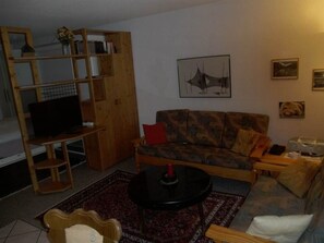 A living room with a sofa, a coffee table, a TV, and a bookshelf. - Valère Leukerbad # 2-bed apartment, Dusche, WC by Interhome (Leukerbad)