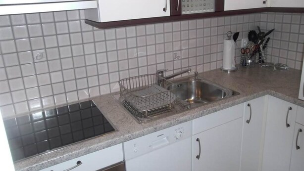 Una cocina con armarios blancos, un lavamanos de acero inoxidable y un escurreplatos.