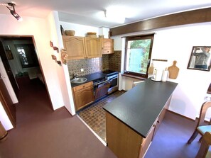 Een compacte keuken met houten kastjes, een ingebouwde kookplaat en een groot raam.