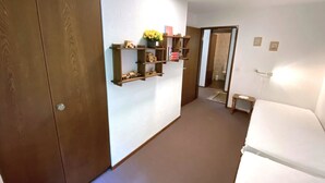 A hotel room with a wardrobe, a bedside table, a small shelf with decorative items, and a door leading to another room. - Lärchenwald 1803 # 5-bed apartment, Bad, WC 5-Bettwohnung, Bad, WC by Interhome (Leukerbad)