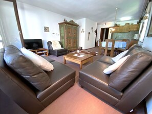 A living room with two leather sofas, a television, a cabinet, and a dining area with a table and chairs. - Lärchenwald 1803 # 5-bed apartment, Bad, WC 5-Bettwohnung, Bad, WC by Interhome (Leukerbad)