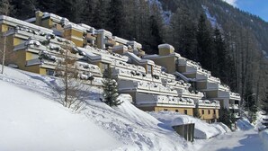 A snow-covered mountain resort with multi-story buildings, a ski slope, and dense forest in the background. - Lärchenwald 1803 # 5-bed apartment, Bad, WC 5-Bettwohnung, Bad, WC by Interhome (Leukerbad)