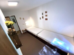 Een kamer met een bed, een klein tafeltje, een wandlamp en een deur versierd met een bloemstuk.
