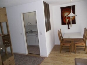 A room with a dining table, chairs, a hanging light fixture, a painting, and a kitchen visible through an open door. - Valère Leukerbad # 2-bed apartment, Dusche, WC by Interhome (Leukerbad)
