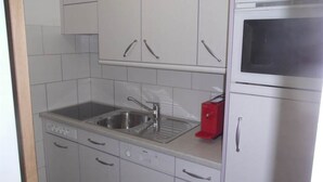 Una cocina con armarios blancos, un lavamanos de acero inoxidable, un tostador rojo y un microondas.