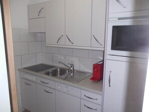 A kitchen with white cabinets, a stainless steel sink, a red toaster, and a microwave. - Valère Leukerbad # 2-bed apartment, Dusche, WC by Interhome (Leukerbad)