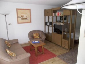 Ein Wohnzimmer mit einer Couch, einem Sessel, einem Couchtisch, einem Bücherregal und einem gerahmten Bild an der Wand.