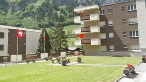 Un edificio moderno con varios balcones, una bandera y un paisaje montañoso al fondo.