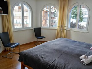 A hotel room with a bed, two chairs, and large windows with curtains. - Edelweiss C 31 # 4-bed apartment, Dusche, WC 4-Bettwohnung, Dusche, WC by Interhome (Leukerbad)