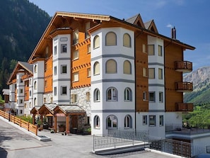 A multi-story hotel with a stone facade, wooden balconies, and a reception area. - Edelweiss C 31 # 4-bed apartment, Dusche, WC 4-Bettwohnung, Dusche, WC by Interhome (Leukerbad)