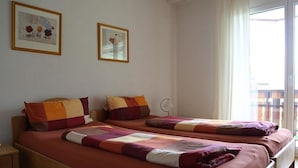 Habitación de hotel con dos camas, cada una con un edredón de diferente color, una mesita de noche y una ventana con cortinas.