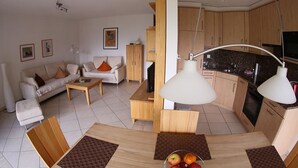 Una sala moderna con un sofá, una mesa de centro y un comedor con una mesa y sillas. Cuenta con una cocina con armarios y estufa.