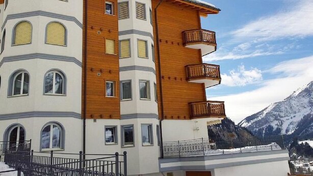 Un edificio de varios pisos con balcones, amplias ventanas y un paisaje montañoso al fondo.