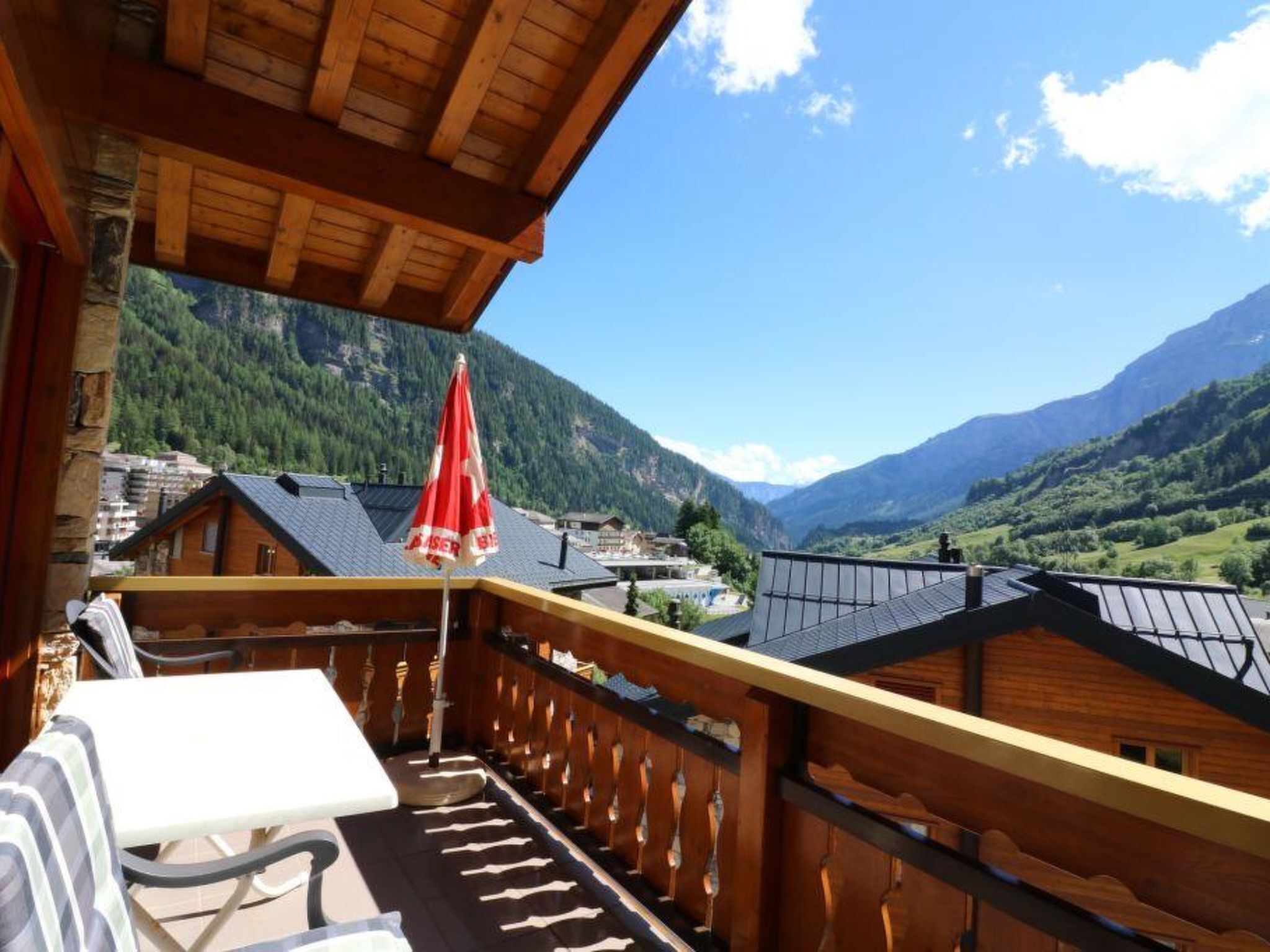 A wooden balcony with a table and chairs, overlooking a mountainous landscape.