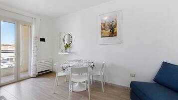 Une pièce comprenant une table à manger, des chaises, un canapé bleu, un radiateur, un miroir et un tableau accroché au mur.