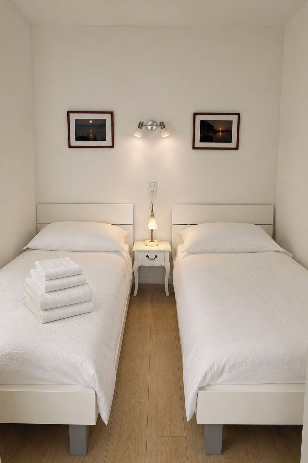 Ein Hotelzimmer mit zwei Betten, einem Nachttisch mit Lampe und zwei gerahmten Bildern an der Wand.