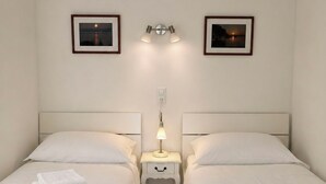 Una camera d'albergo con due letti, un comodino con una lampada e due quadri appesi al muro.