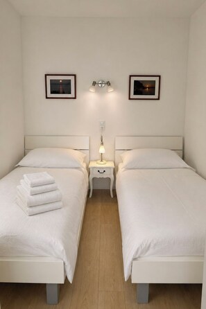 Ein Hotelzimmer mit zwei Betten, einem Nachttisch mit Lampe und zwei gerahmten Bildern an der Wand.
