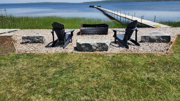 Ein Sitzbereich am Seeufer mit Adirondack-Stühlen, einem Feuerkorb und einem Steg, der ins Wasser ragt.