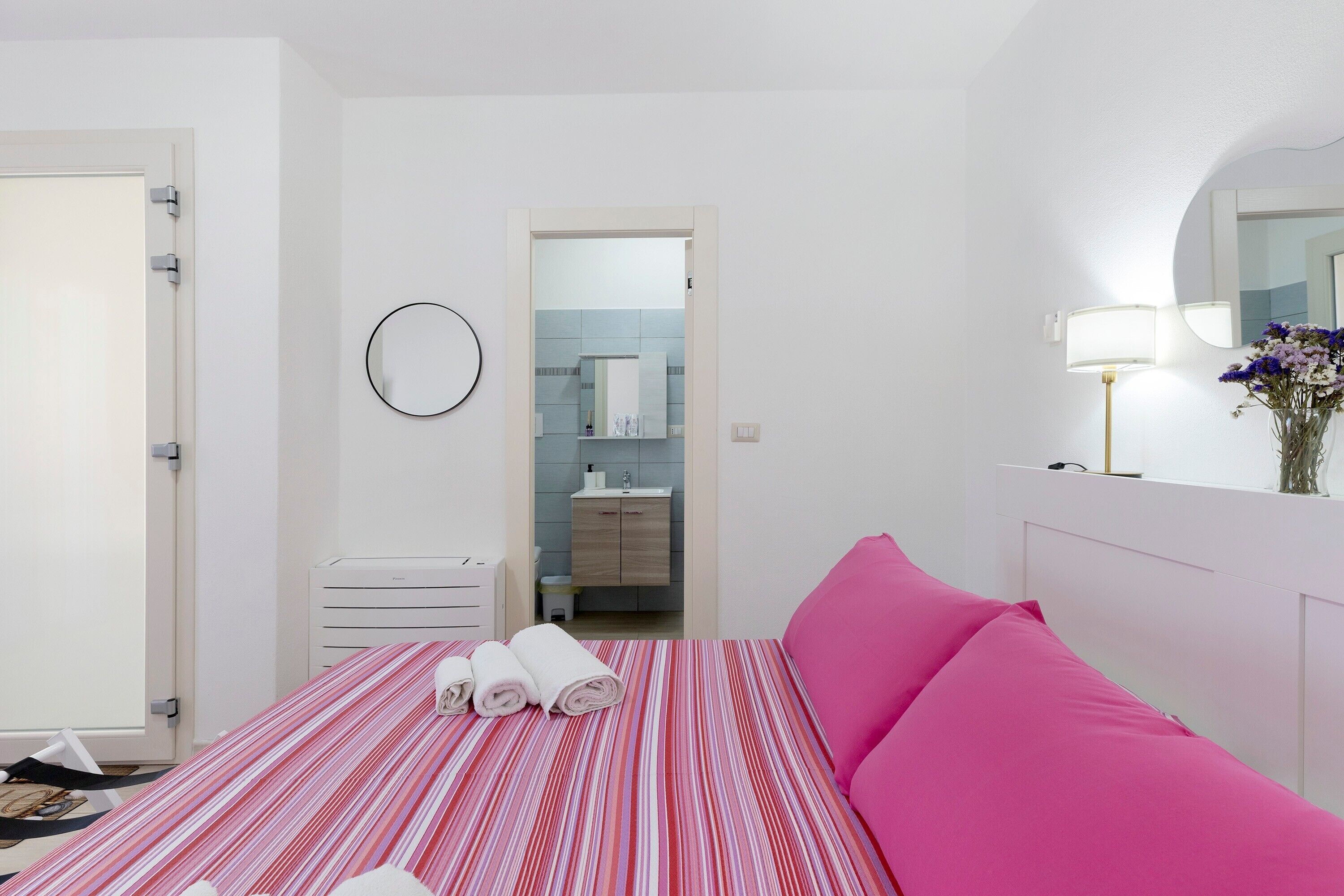 Une chambre d’hôtel avec un lit, une table de chevet, une lampe et une salle de bain visible à travers une porte ouverte.