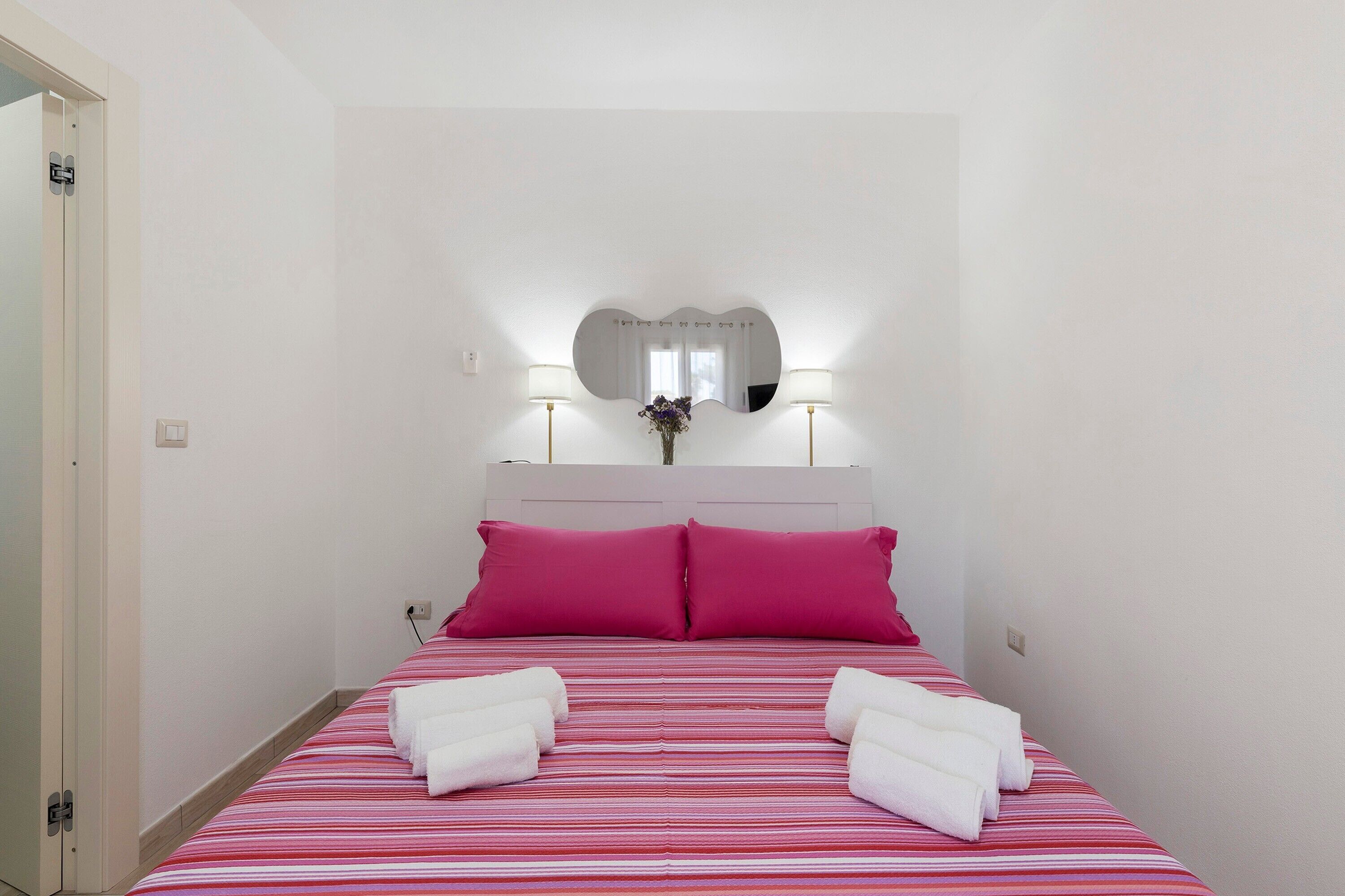 Een hotelkamer met een bed, twee kussens, een bedlampje en een spiegel aan de muur.