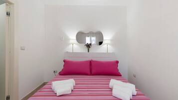 Een hotelkamer met een bed, twee kussens, een bedlampje en een spiegel aan de muur.