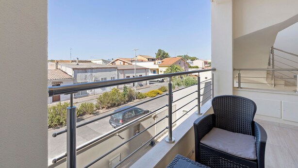A balcony with a wicker chair, a metal railing, and a view of buildings and a street.