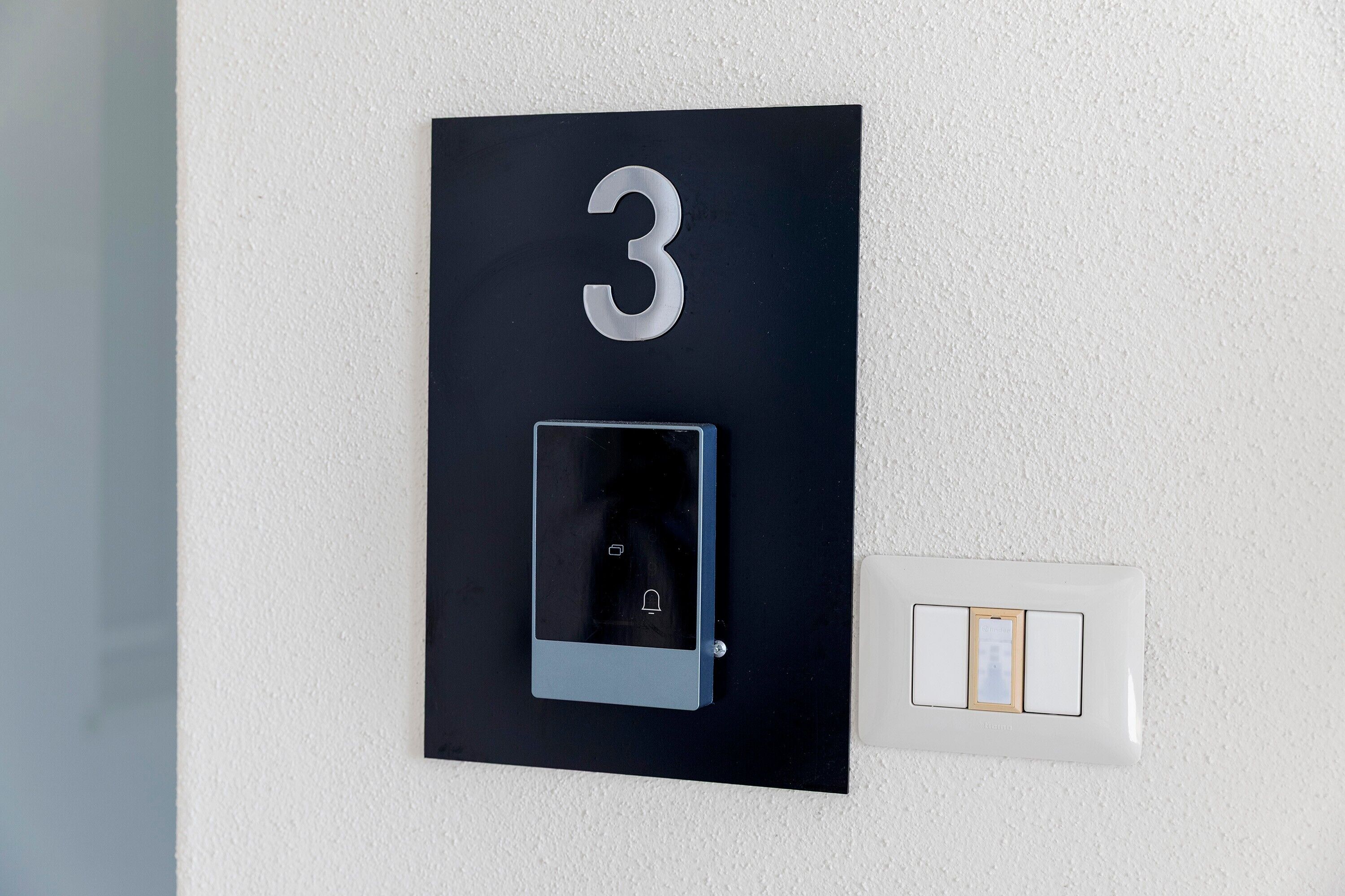 Una placa con el número 3, una cerradura digital y un interruptor de luz, todo montado en la pared.