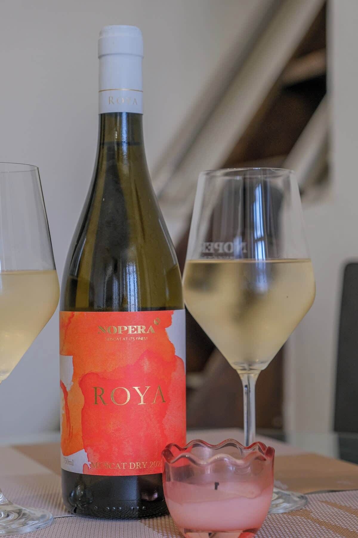 En flaska ROYA-vin, ett glas vitt vin och en rosa drink på ett bord.