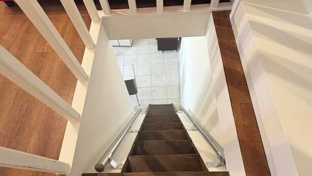 Una escalera de madera con barandillas blancas y una zona acolchada de color rojo en la parte superior.
