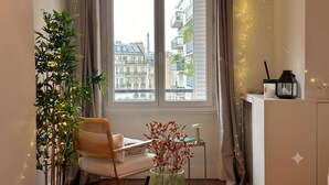 Ein gemütliches Zimmer mit Blick auf Paris, ausgestattet mit einem Sessel, einem kleinen Tisch und einer Zimmerpflanze.