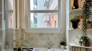Eine moderne Küche mit Fenster, weißen Schränken, einem Edelstahlkühlschrank und einer Pendelleuchte.