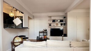 Ein modernes Wohnzimmer mit einem Ecksofa, einem Flachbildfernseher, Regalen mit Dekoration und einem Globus auf einem Beistelltisch.