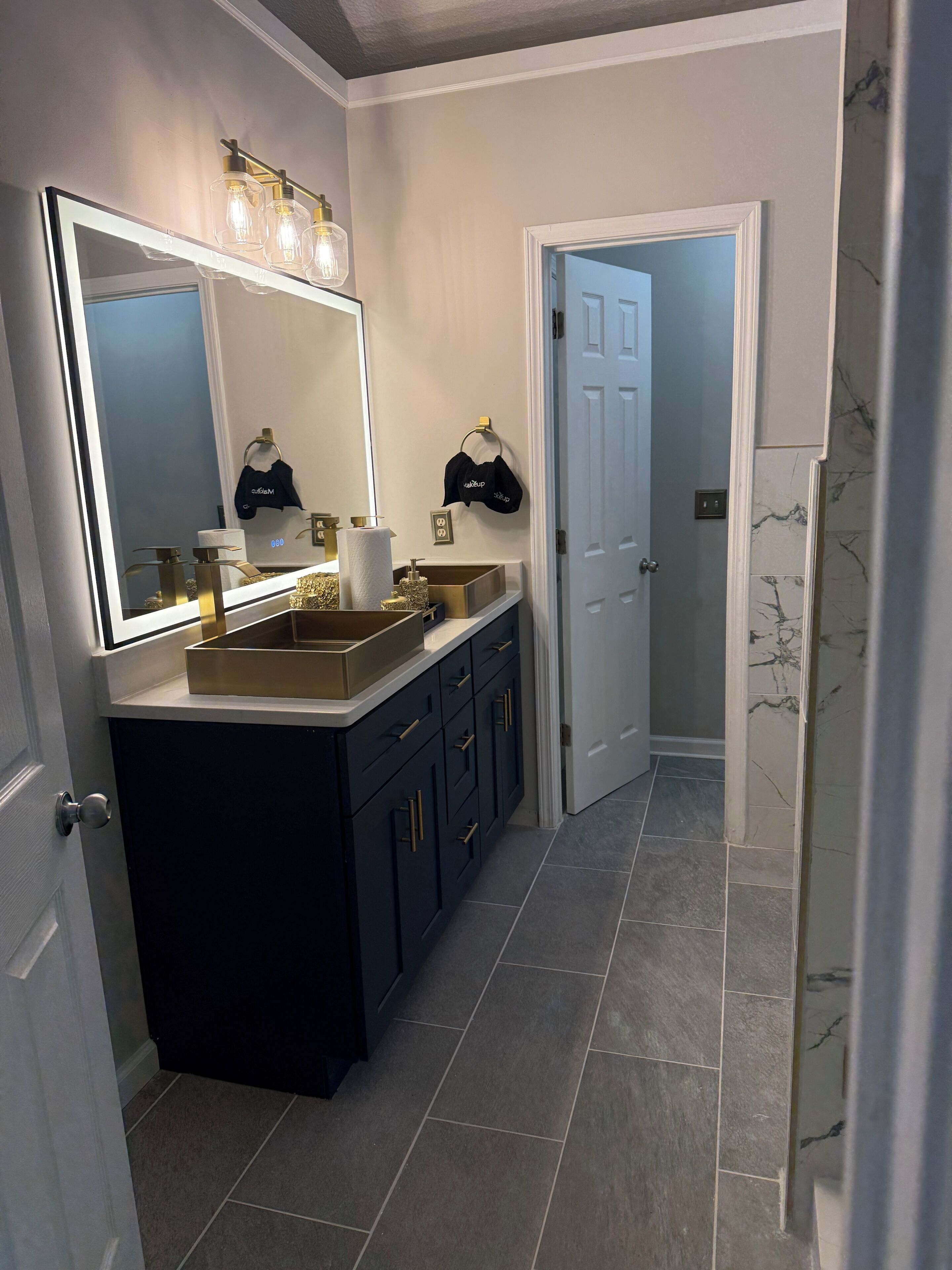 A bathroom with a large mirror, vanity, and a door leading to another room.