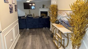 A modern living room with a dark blue sofa set, a flat-screen TV mounted on the wall, a ceiling fan, and a decorative plant arrangement. - Bleu et Doré (Atlanta)