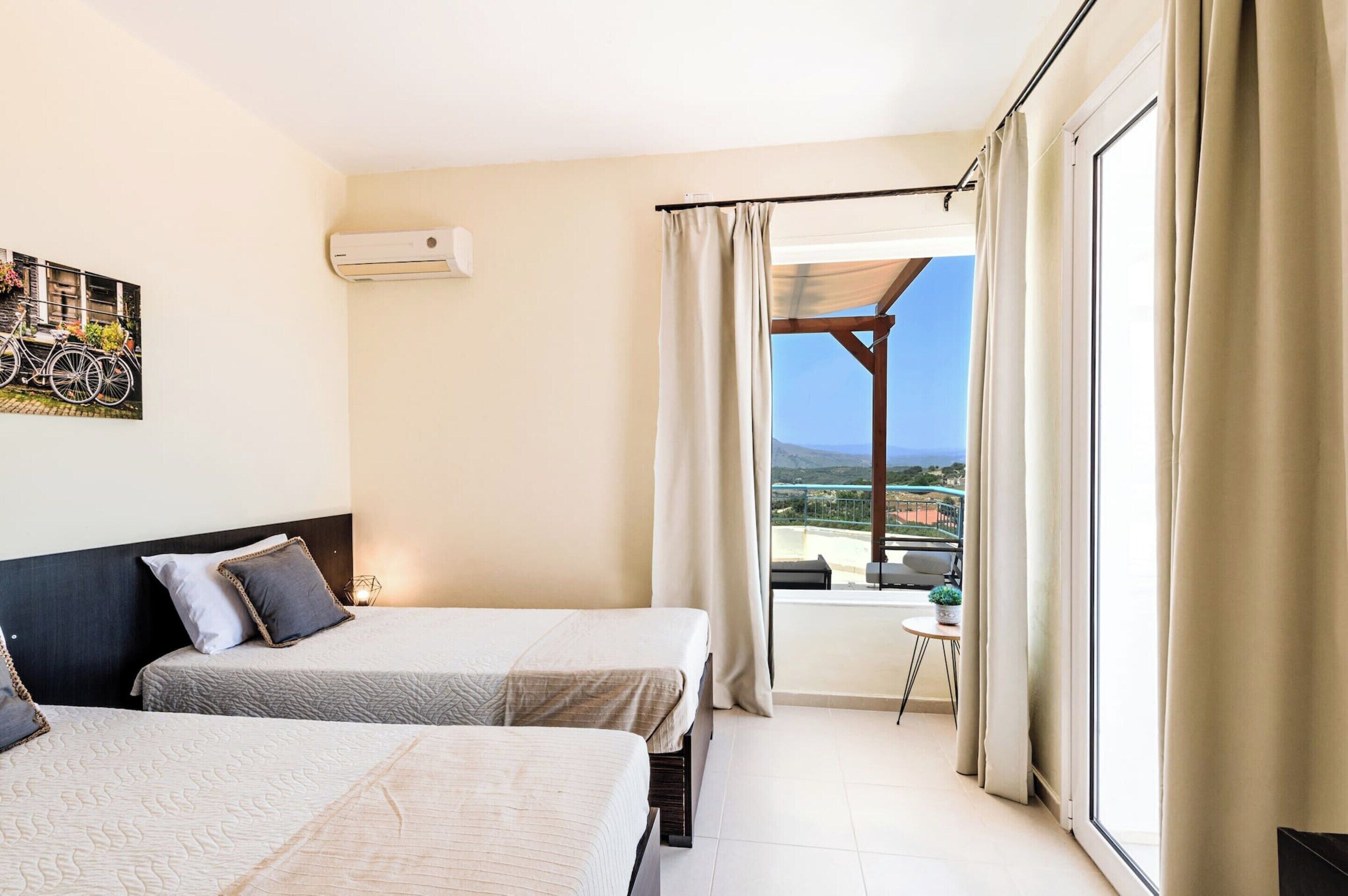 A hotel room with two beds, a balcony with a view, and a painting on the wall.
