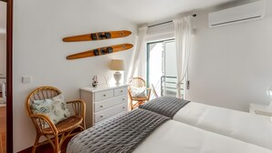 Ein Schlafzimmer mit einem Bett, zwei Stühlen, einem Schminktisch und einer Lampe. An der Wand sind zwei Ski zu sehen.