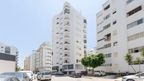Ein mehrstöckiges Wohngebäude mit Balkonen, ein Parkplatz mit mehreren Autos und ein Baum im Vordergrund.