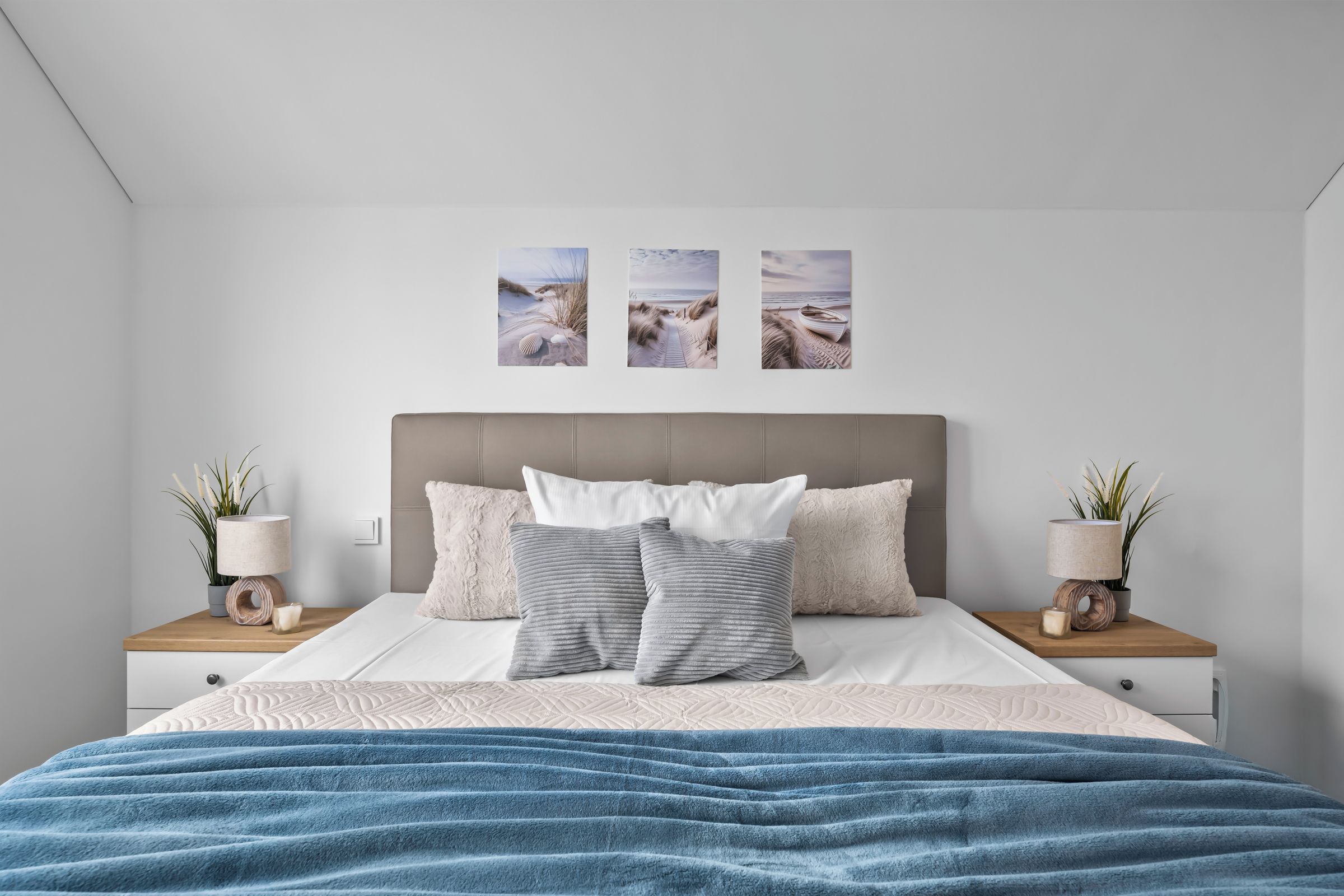 Une chambre à coucher avec un lit, des oreillers, une couverture bleue et des œuvres d’art murales.