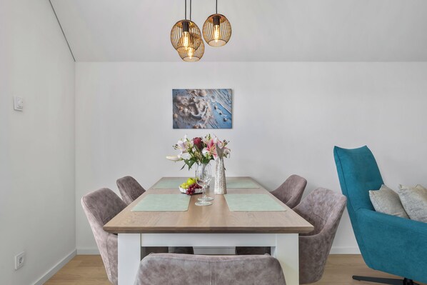 A dining area with a wooden table, cushioned chairs, a vase with flowers, and a painting on the wall. - Perfekte Welle - balcony, electric car charging station, private parking (Kappeln)