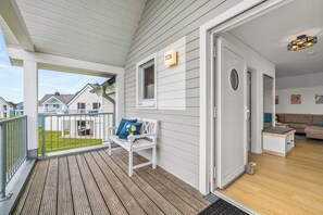 Ein Wohnhaus mit einer Holzterrasse, einer weißen Bank und einer Tür zu einem Wohnbereich.