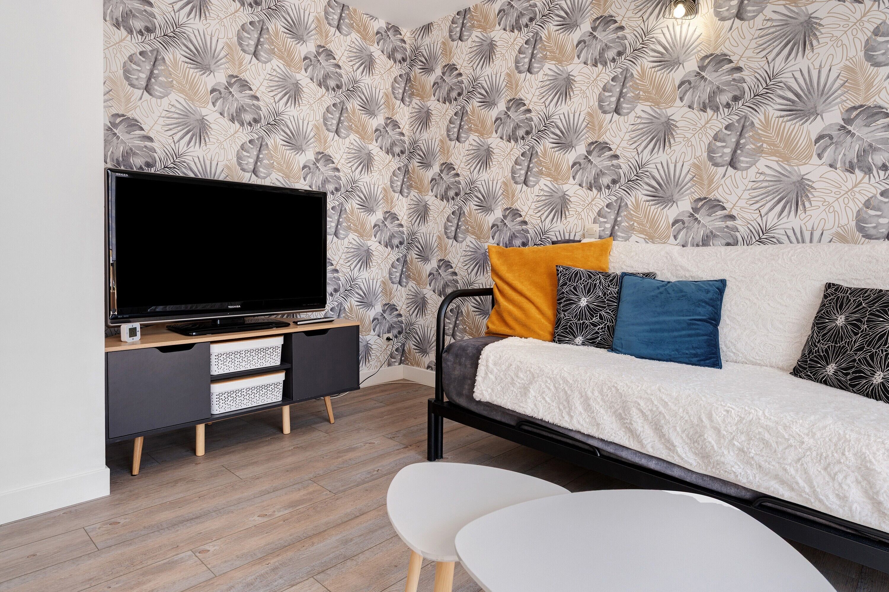 A modern room with a flat-screen TV, a bed with multiple pillows, a small white table, and a wooden floor.